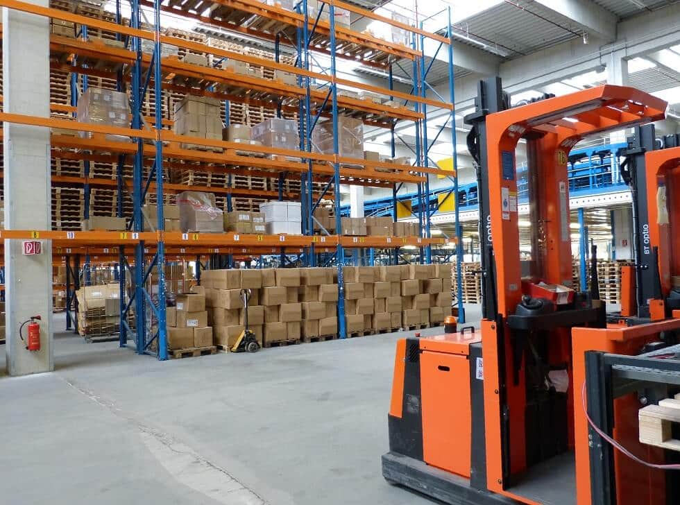 Warehouse with orange pallet racks stacked with boxes and reach-truck forklifts