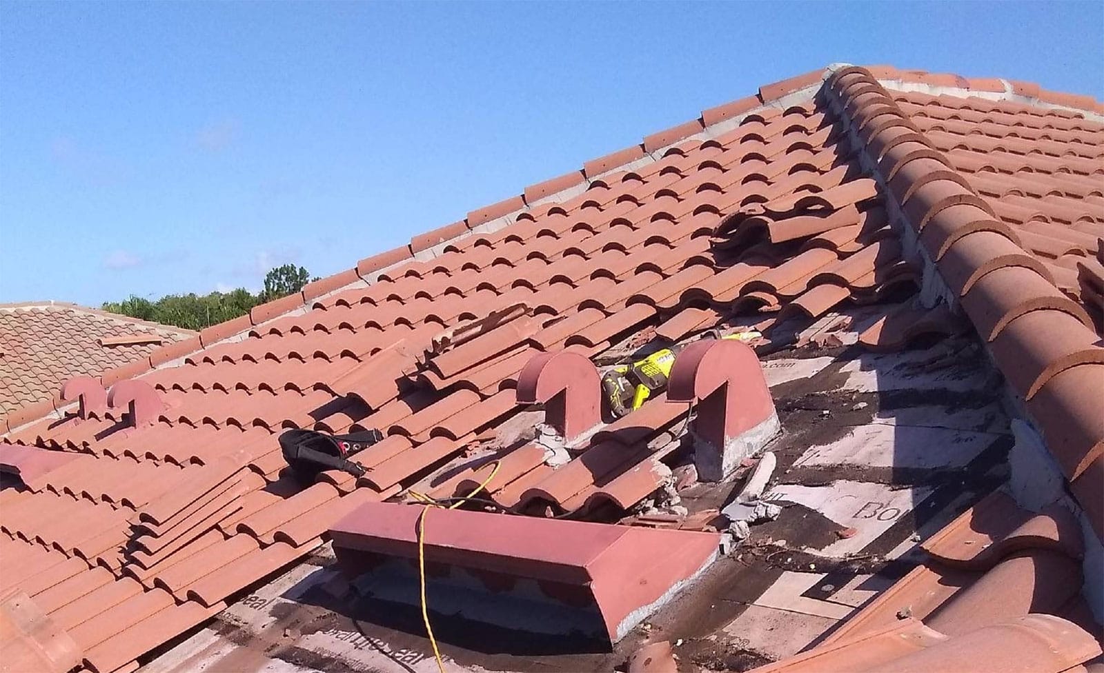 Storm-damaged clay tile roof with lifted tiles and exposed underlayment