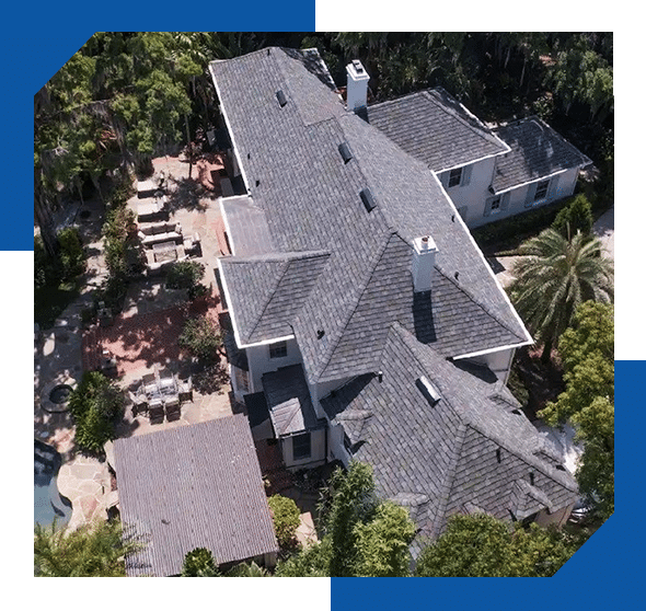 Aerial view of a large home with a gray flat concrete tile roof among palm trees