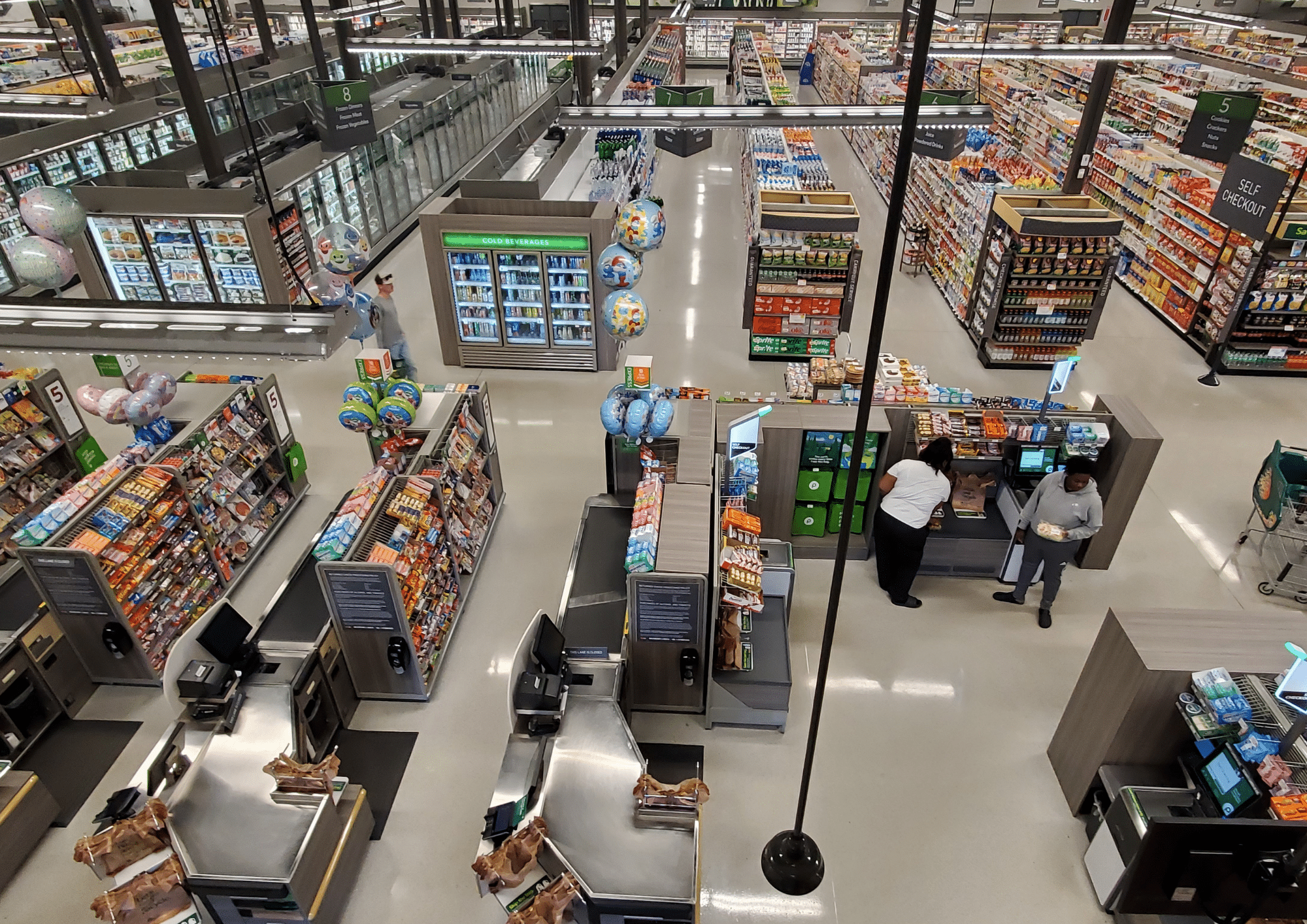 Overhead view of a grocery store interior with aisles, coolers and self-checkout lanes