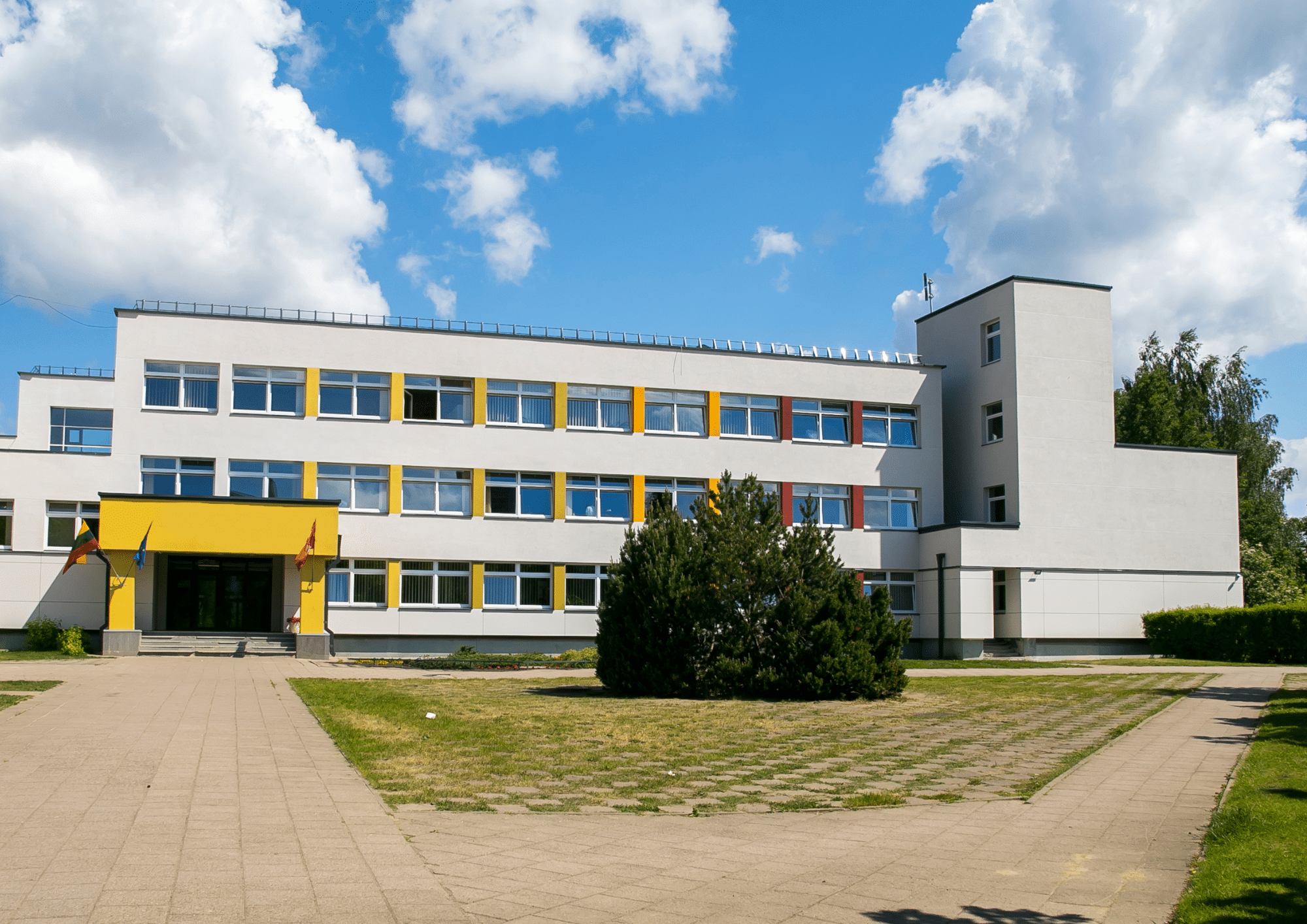 Three-story school building with a yellow entrance canopy and a courtyard lawn