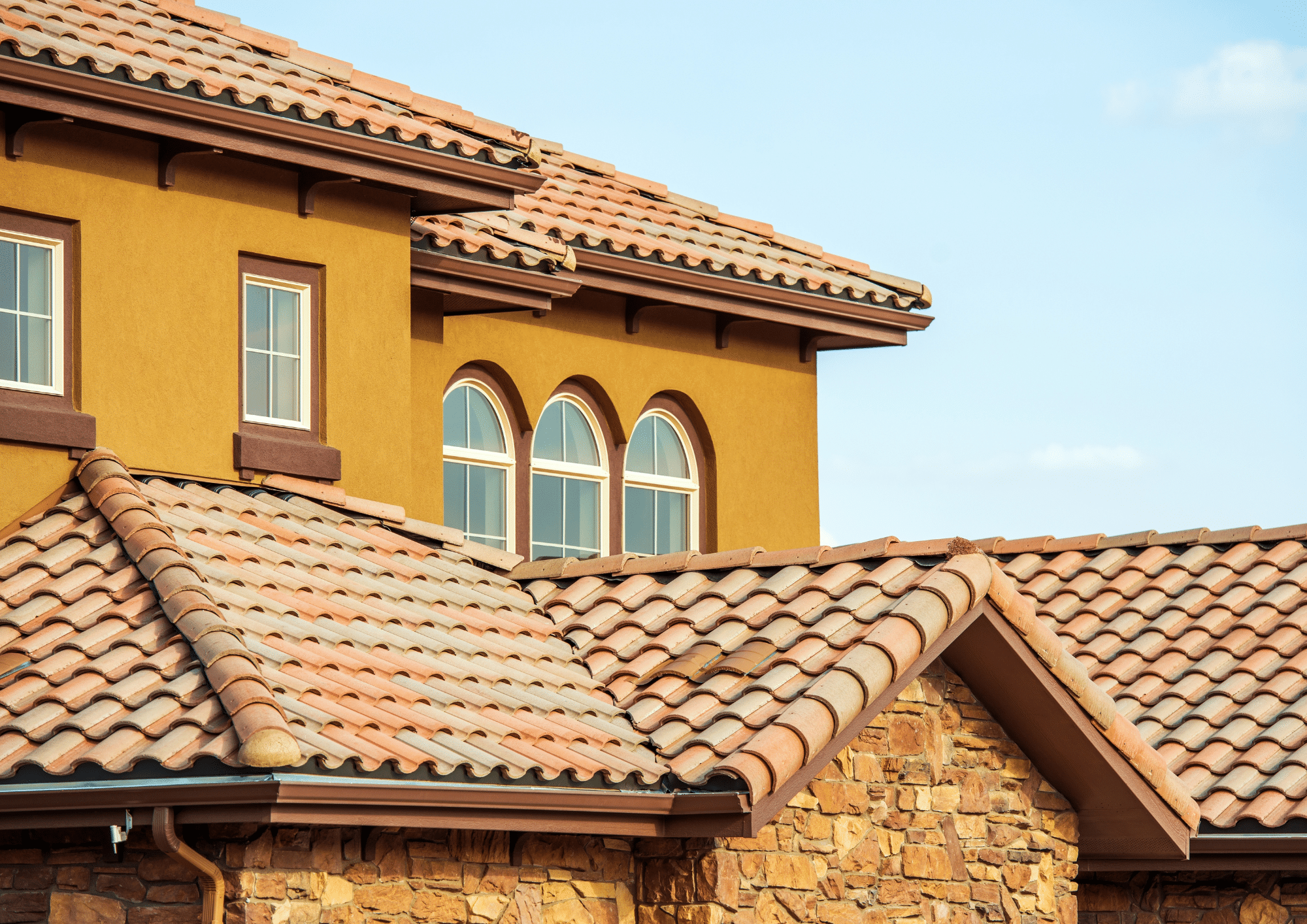 Terracotta clay tile roof on a two-story stucco home with arched windows and stone accents