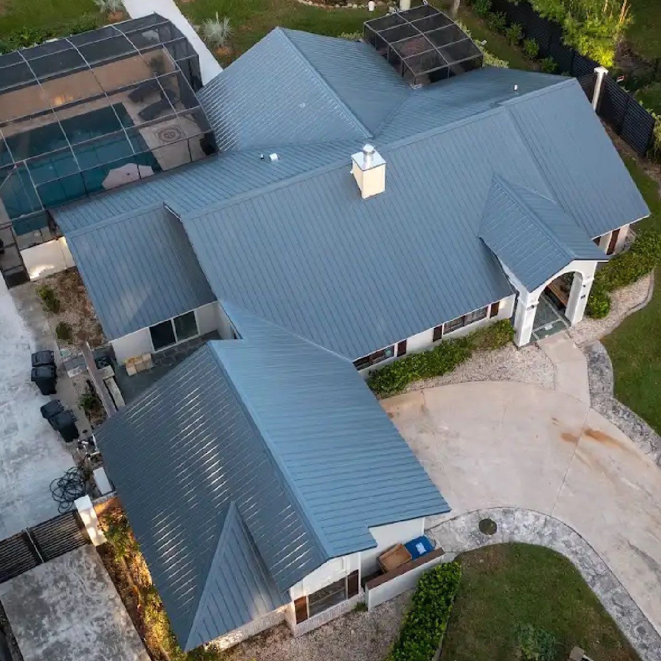 Aerial view of a home with a new blue-gray standing seam metal roof and a screened pool enclosure