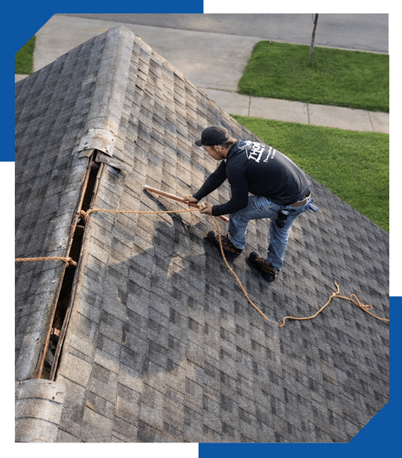 Roofer in a Thomas Roofing shirt inspecting a weathered asphalt shingle roof with a section of ridge cap removed
