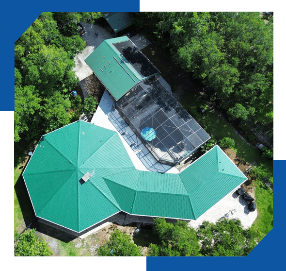 Aerial view of a home and outbuilding with green metal roofs and a screened pool enclosure among trees
