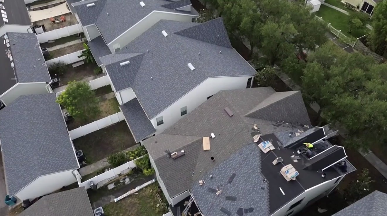 Aerial view of townhome roofs with one shingle roof replacement in progress, bundles staged on the roof