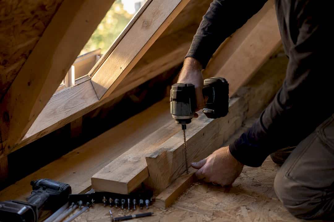 Hands installing structural screws in attic rafters